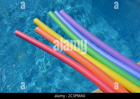 Rainbow coloured pool noodles floating in a swimming pool on a bright and sunny day Stock Photo