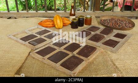 Handmade chocolate blocks inside wooden molds, ripe cocoa fruits and glass jars with cocoa products on a jute covered table Stock Photo