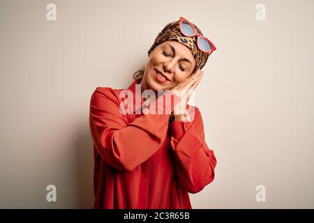 Middle age brunette woman wearing handkerchief on head and shirt over white background sleeping tired dreaming and posing with hands together while sm Stock Photo