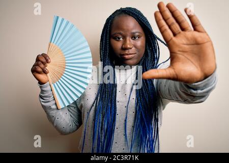 Young african american plus size woman with braids using hand fan over white background with open hand doing stop sign with serious and confident expr Stock Photo