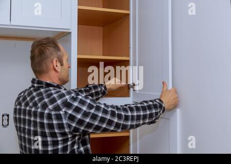 Master adjusts fixing in the hinge of the kitchen cabinet door with screwdriver. Stock Photo