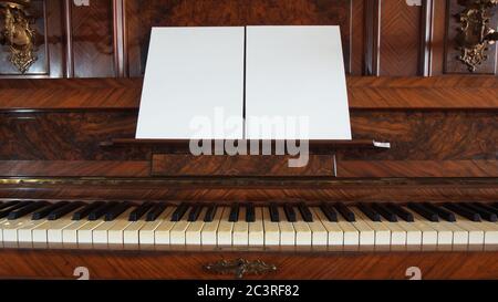 Front view of an antique wooden piano with the keyboard open and two sheets of blank paper on support for musical notes Stock Photo