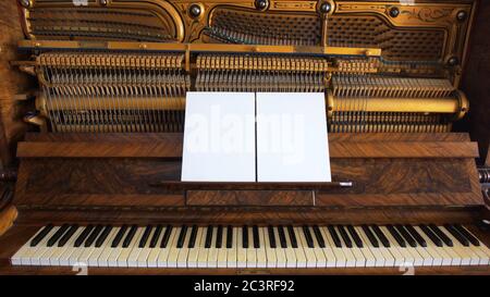 Front view of an antique wooden piano with the keyboard open and two sheets of blank paper on support for musical notes Stock Photo