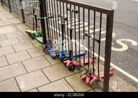 children's scooters tied up outside school, London, UK Stock Photo