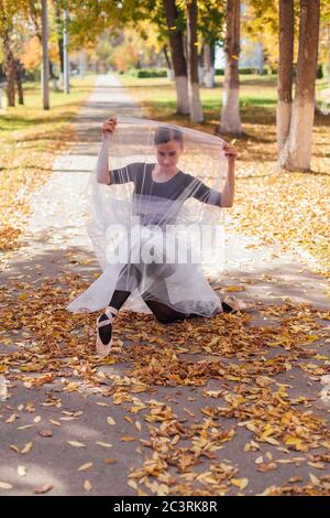 Woman ballerina in a white ballet skirt dancing in pointe shoes in a golden autumn park on dry yellow leaves. Stock Photo