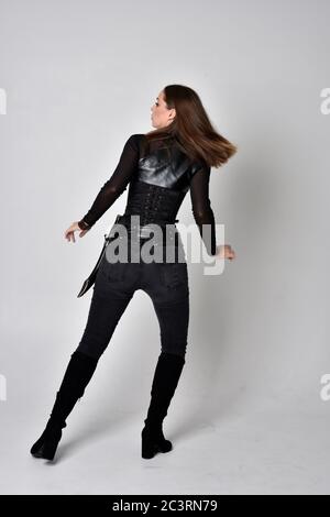 Portrait of brunette girl wearing black leather catsuit.  full length standing pose, isolated against a studio background. Stock Photo