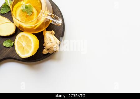 top view of hot tea in teapot served on wooden board with ginger root, lemon and mint on white background Stock Photo