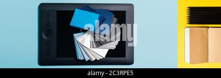 Collage of color samples on graphics tablet and notebook with pencils on blue and yellow background Stock Photo