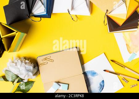 top view of paintbrushes, clips, paintings, blank notebook, flower and colorful palette on yellow Stock Photo