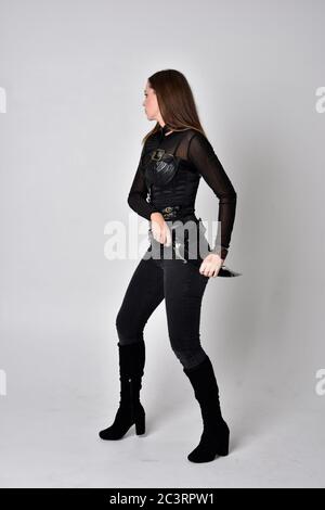 Portrait of brunette girl wearing black leather catsuit.  full length standing pose, isolated against a studio background. Stock Photo