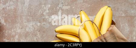 top view of paper bag with bananas on beige weathered surface, panoramic crop Stock Photo