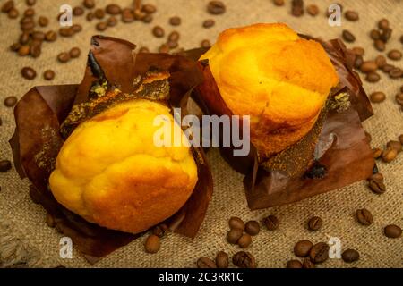 Two fresh cupcakes and coffee beans on a rough-textured homespun fabric. Close up Stock Photo