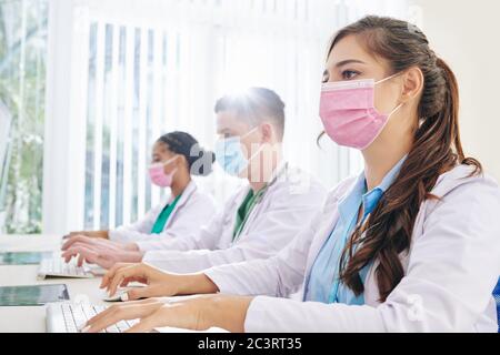 Young doctors in medical masks working on computers in office Stock Photo