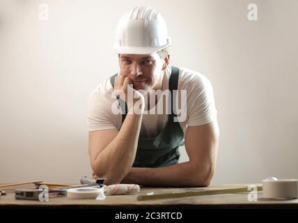 Middle-aged carpenter wearing a white hard hat and uniform against a white wall Stock Photo