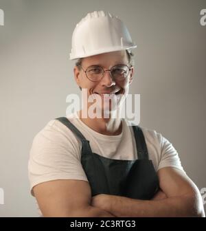 Middle-aged carpenter wearing a white hard hat and uniform against a white wall Stock Photo