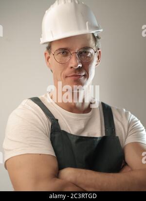 Middle-aged carpenter wearing a white hard hat and uniform against a white wall Stock Photo