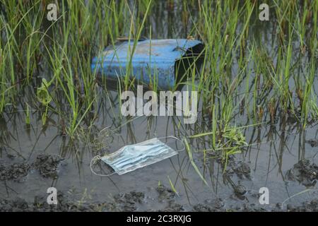 Face mask and plastic debris in the river. Coronavirus is contributing to pollution, as discarded face masks clutter rivers and lakes along with plast Stock Photo