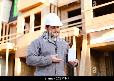 Foreman showing disinfectant at construction site and wearing hardhat. Stock Photo