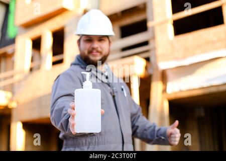 Focus on disinfectant, foreman in hardhat showing thumbs up at construction site. Stock Photo
