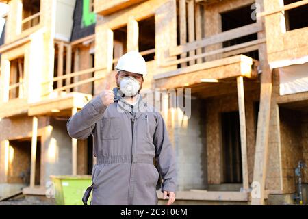 Construction worker wearing respirator near building and showing thumbs up. Stock Photo