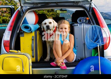 Young girl packs suitcase in the trunk of a car on vacation Stock Photo