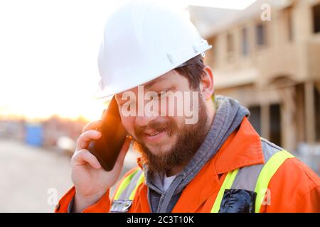Portrait of builder talking by smartphone on construction site. Stock Photo
