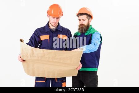 Architects in hard hat on busy faces looks at drawing, plan, project. Builder, engineer, architect work at site. Men in helmets with blueprint on white background. Architect and build concept. Stock Photo