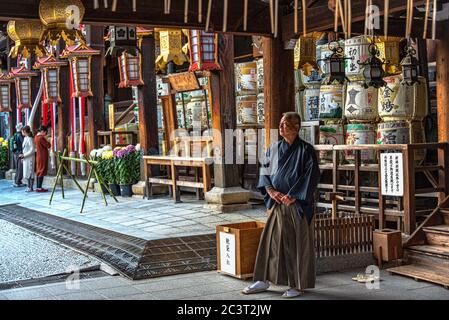 Monk in traditional robes standing in front of altar, Kitano Tenmangu shinto shrine, Kyoto, Japan Stock Photo