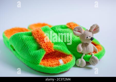 A toy mouse sits on bright fluffy slippers, isolated on a white background. Home women's or children's clothing.The concept of home warmth and comfort Stock Photo