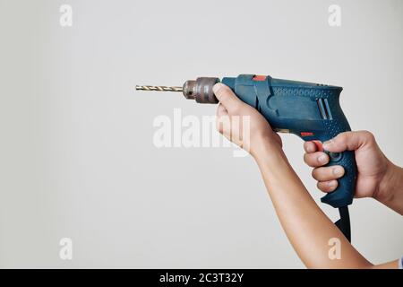 Hands of builder holding electric drill to make holes in wall Stock Photo