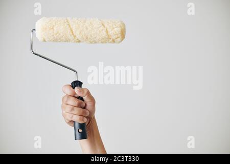 Construction worker holding fluffy roll he is using for application of paint on the wall Stock Photo