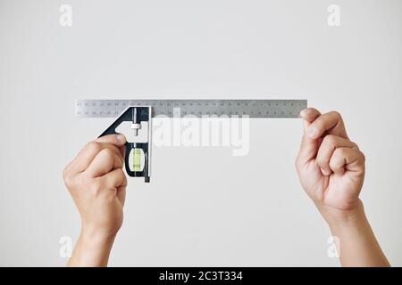 Construction worker or builder attaching spirit level to metal ruler to measure details on site Stock Photo