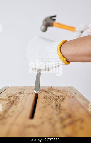 Carpenter in textile gloves using chisel and hammer when making hole in wooden bench Stock Photo