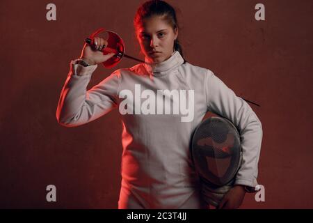 Fencer woman with fencing epee sword on shoulder in red light. Stock Photo