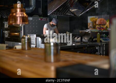 Restaurant professional open kitchen, Woman in a mask on her face, new measures to fight the virus Stock Photo