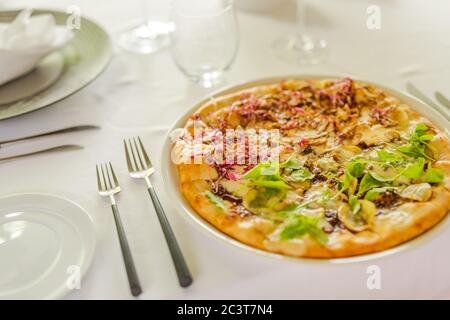 Traditional Italian pizza in pizzeria in Milan. Elegant white table top set-up in luxury restaurant, gourmet vegan pizza Stock Photo