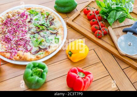 Freshly baked pizza with fresh vegetables, food ingredients, vegan pizza om wooden table top. Stock Photo
