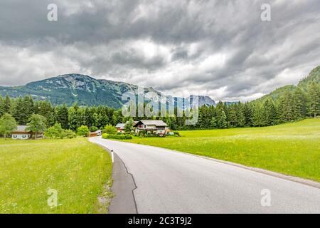 Alpine landscape with road under cloudy sky. Mountain pass, pine forest Stock Photo