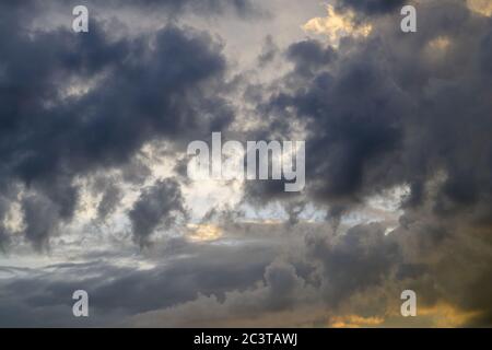 Dramatic sunset with stormy dark clouds in the foreground opening to a colorful orange sky behind in full frame Stock Photo