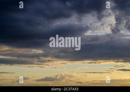 Dramatic sunset with stormy dark clouds in the foreground opening to a colorful orange sky behind in full frame Stock Photo