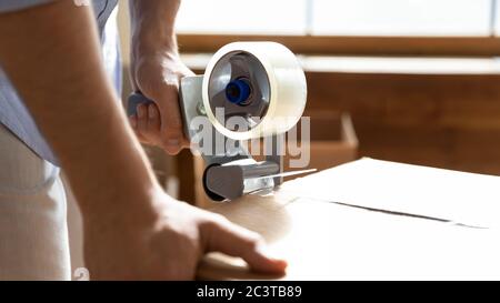 Close up man using adhesive tape dispenser, packing box Stock Photo