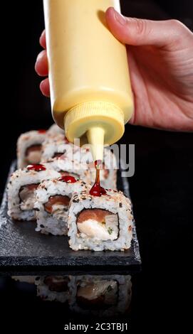 Delicious sushi roll served on black slate. In the frame, the hand of a chef pouring food with sweet sauce. Stock Photo