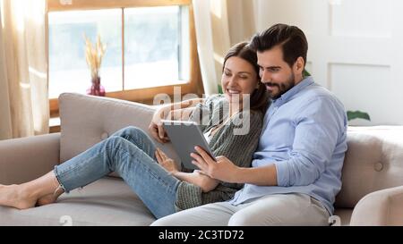 Happy young couple relaxing on couch, using computer tablet together Stock Photo