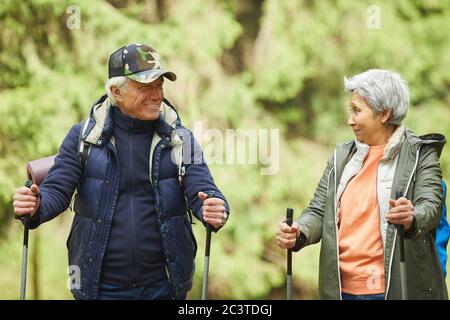 Waist up portrait of cheerful senior couple enjoying Nordic walking with poles during hike in forest Stock Photo