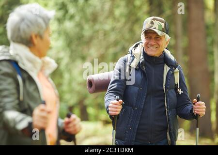 Waist up portrait of active senior man enjoying Nordic walking during hike in forest with wife, copy space Stock Photo