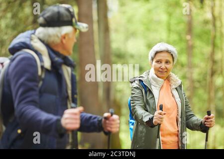 Waist up portrait of active senior woman enjoying Nordic walking during hike in forest with husband, copy space Stock Photo