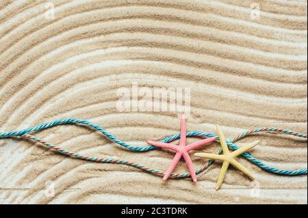 Two colored starfish and two colored marine ropes on textured wavy sand. Top view. Stock Photo