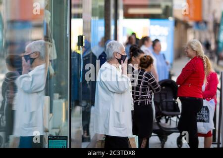 Cardiff, Wales, UK. 22nd June, 2020. The first in the queue outside the newly reopening Next store touches her face mask as some non-essential shops reopen in Cardiff city centre following the coronavirus lockdown. Credit: Mark Hawkins/Alamy Live News Stock Photo