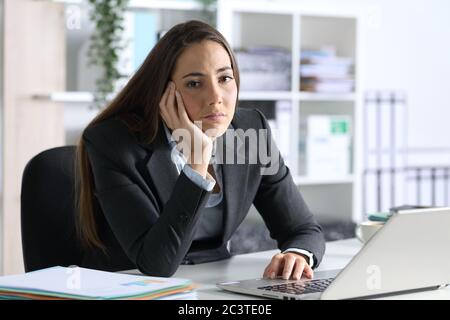 Bored executive woman with laptop looking at camera sitting on her desk at office Stock Photo