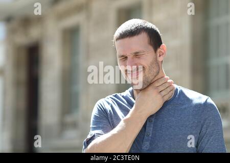Man in pain suffering sore throat standing touching neck in the street Stock Photo